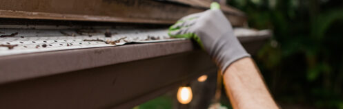 Man clearing leaves and debris from a gutter.